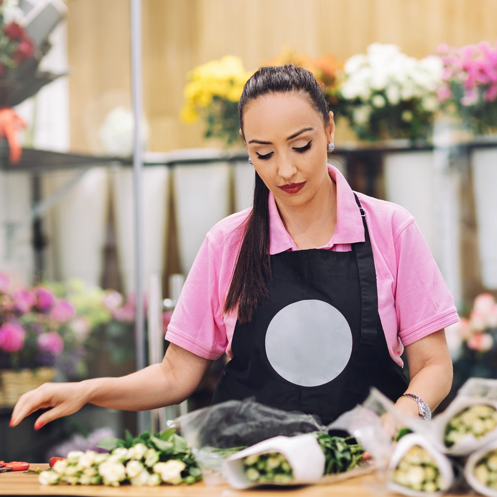 Woman in a pink shirt and black apron working with flowers in a floral shop.