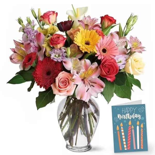 A colorful bouquet of mixed flowers in a clear vase with a &#39;Happy Birthday&#39; card.