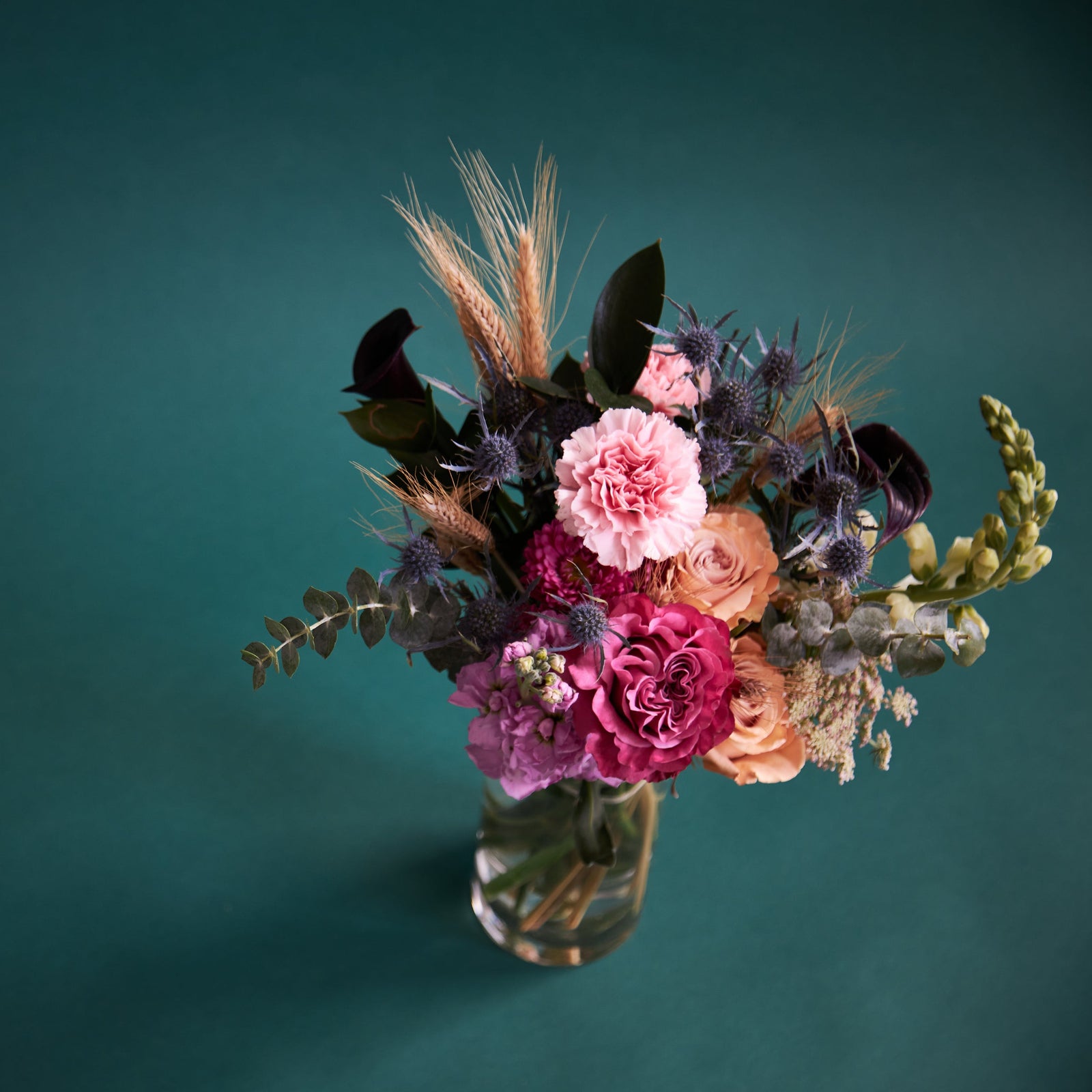 Vivid floral bouquet in clear vase on teal background