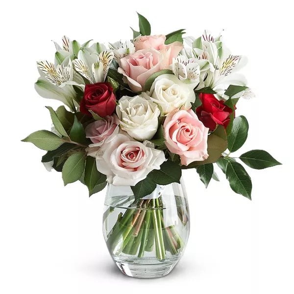 Bouquet of roses in red, pink, and white hues with green leaves in a clear vase.