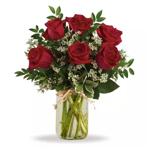 A bouquet of red roses and baby&#39;s breath in a glass jar with a raffia bow.